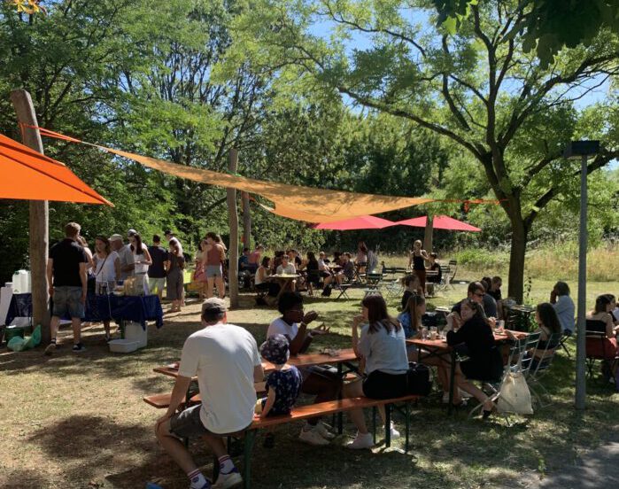 Mehrere Menschen sitzen beim Stadtjugendring im Niedrigseilgarten auf Bänken. Sommerfest